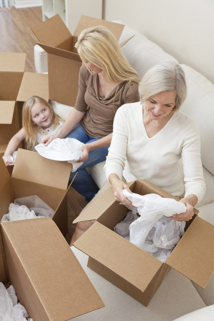 Female generations of a family, mother, daughter &amp; grandmother unpacking boxes and moving into a new home.